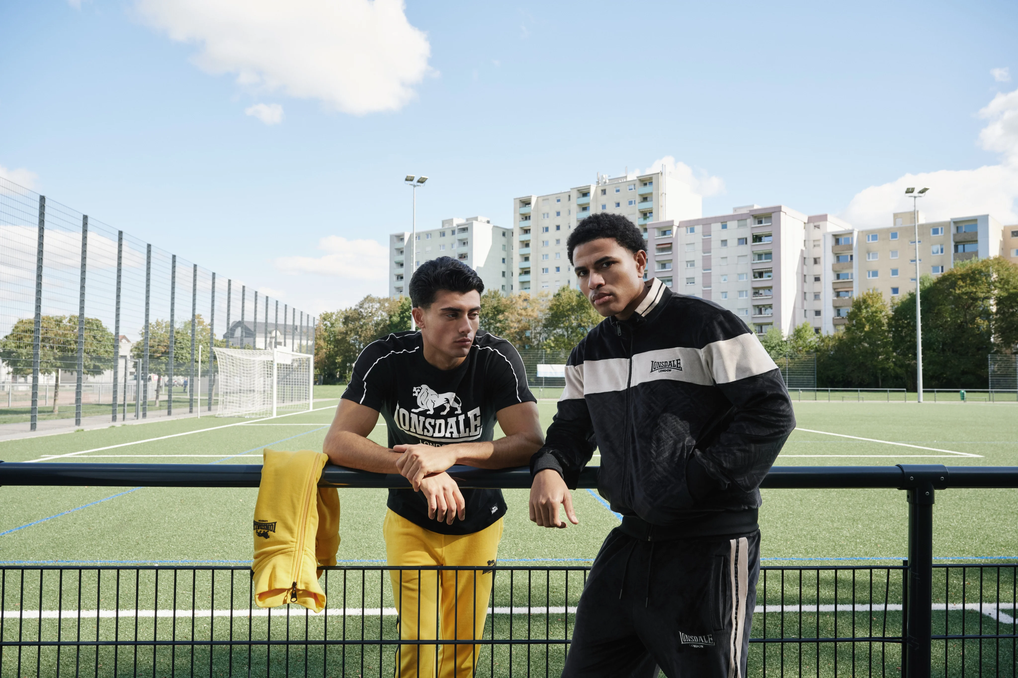 Lonsdale London campaign: two men in Lonsdale sportswear leaning on a railing at a football pitch