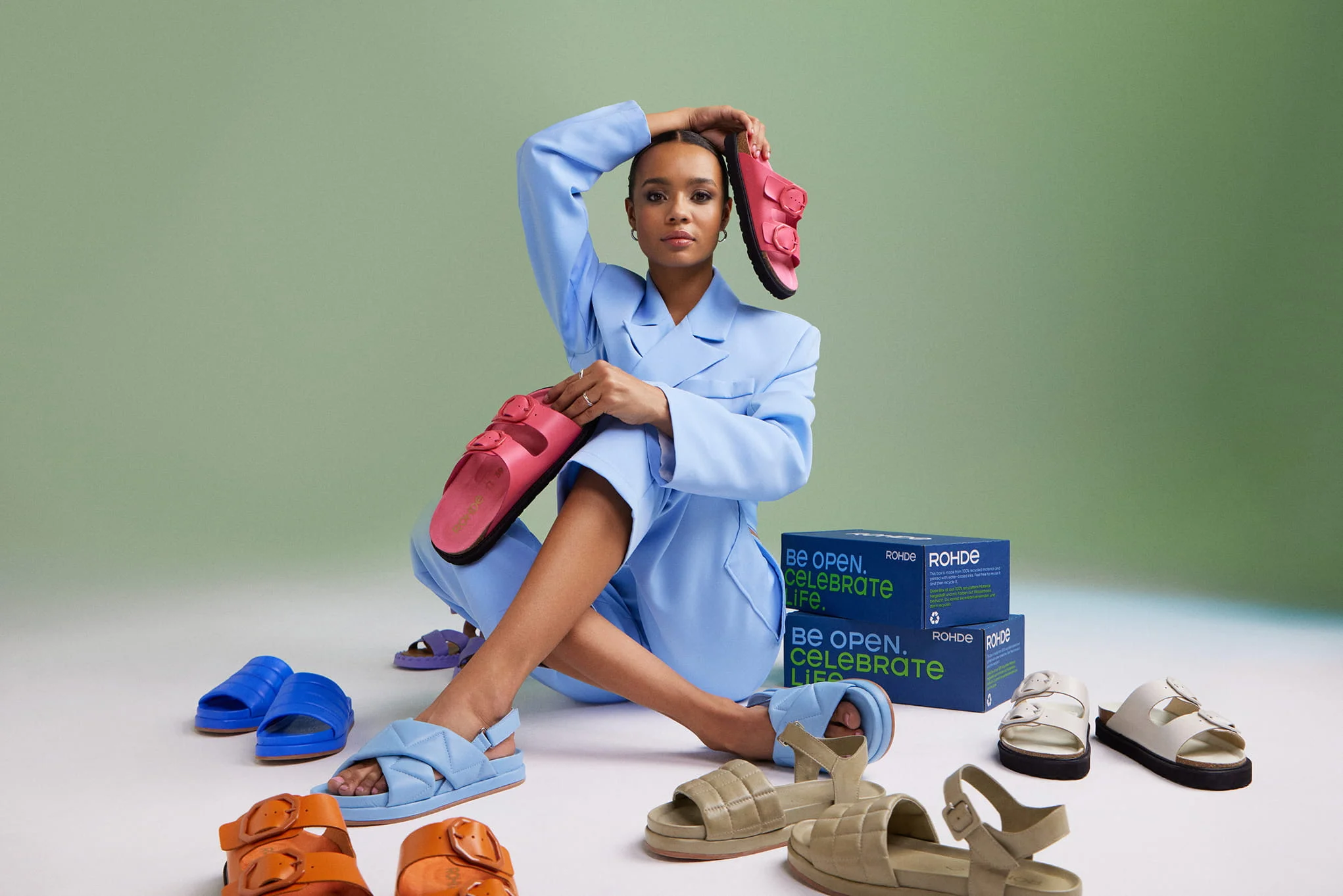 Woman in a light blue suit with sandals in many colors and ROHDE boxes.