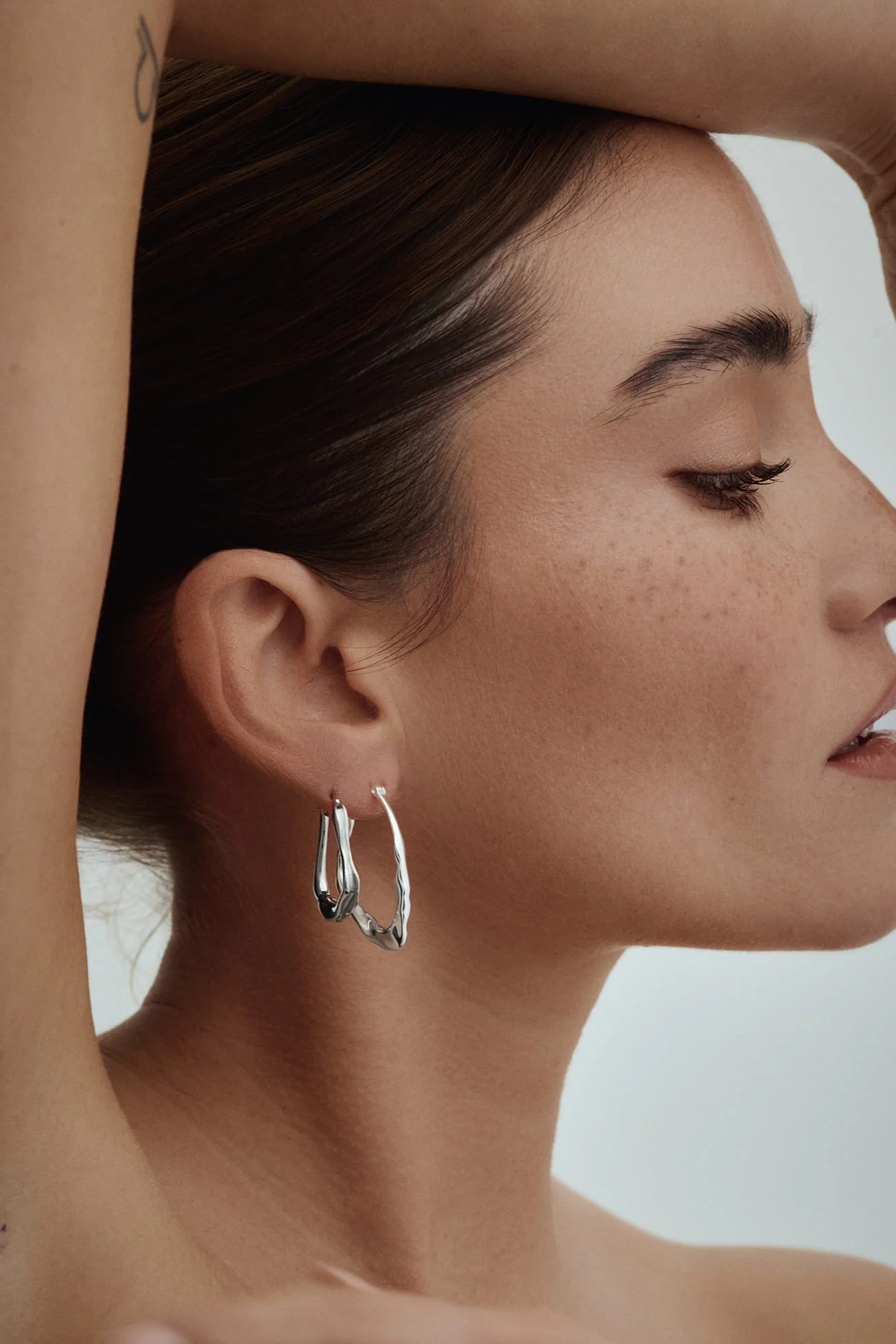 Woman with freckles wearing sculptural silver hoop earrings