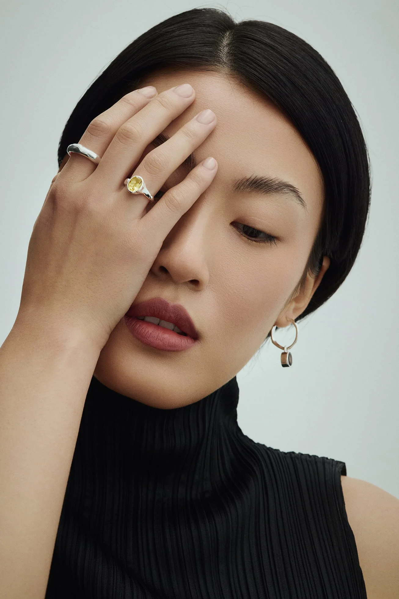Woman covering one eye with her hand, wearing a yellow gemstone ring and hoop earrings