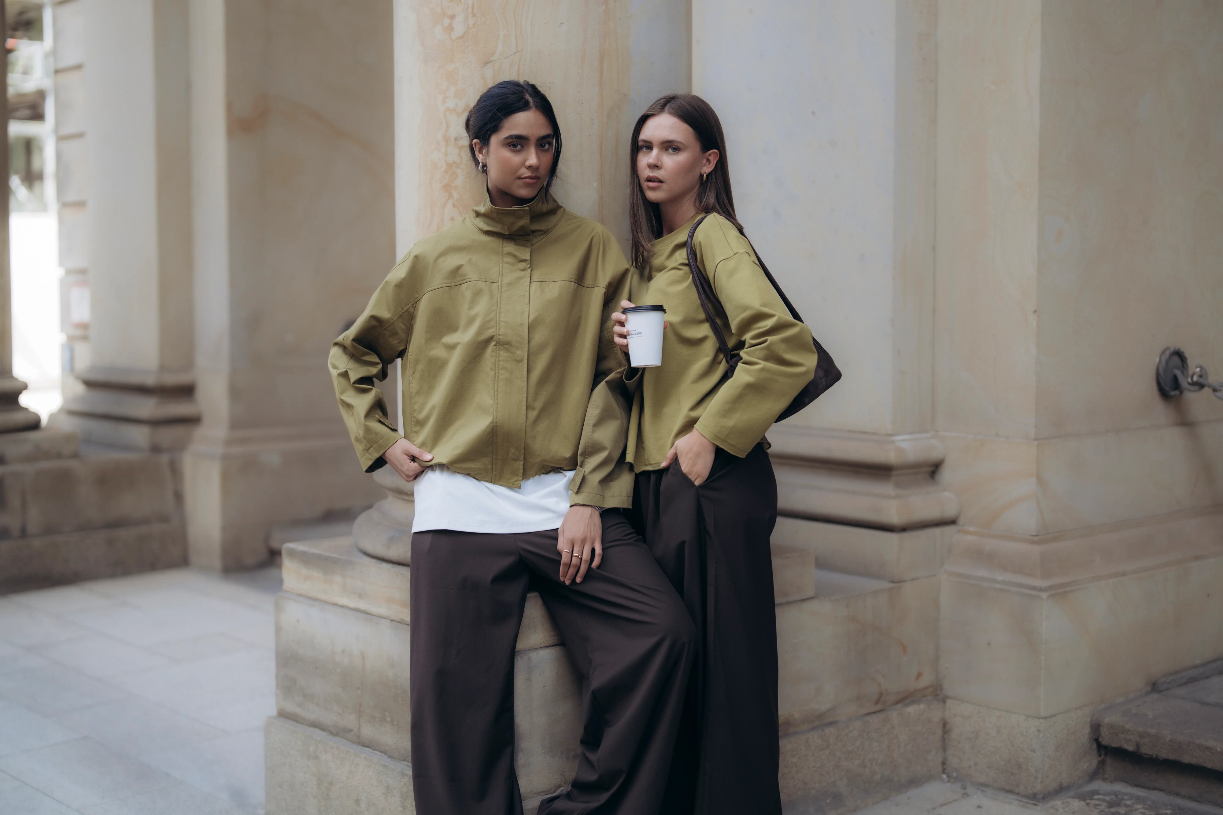 Villa Sophie campaign: two women in olive jackets and wide brown trousers by stone columns