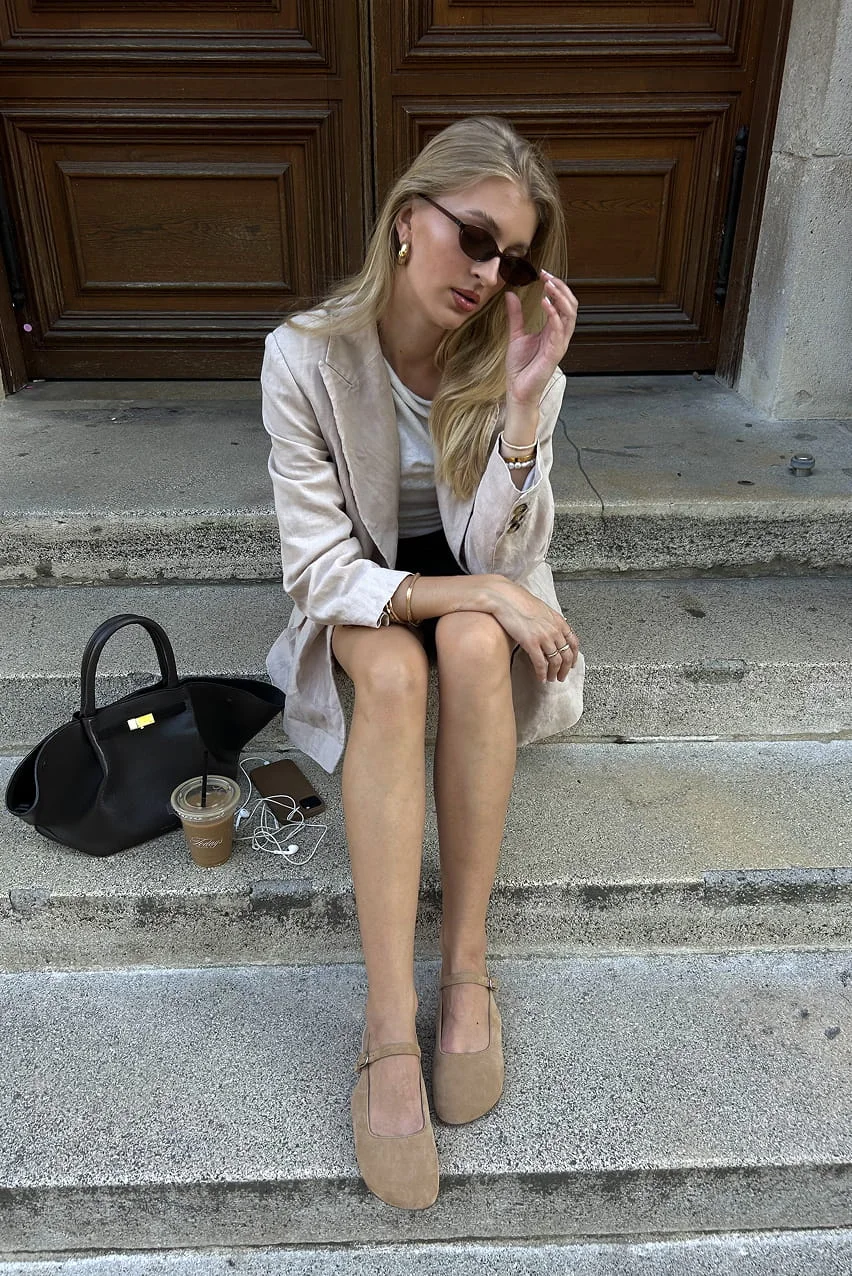 Woman in beige blazer and flats with coffee.