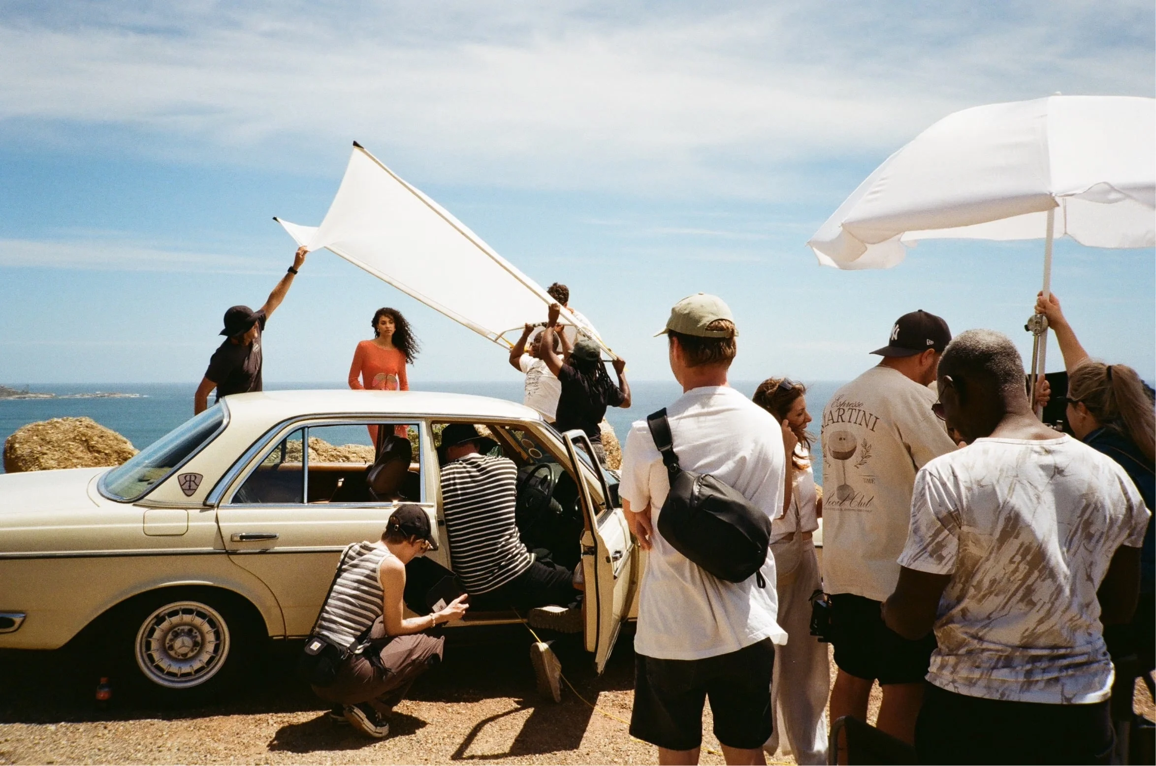 Crew und Models bei einer Strandproduktion mit einem Oldtimer