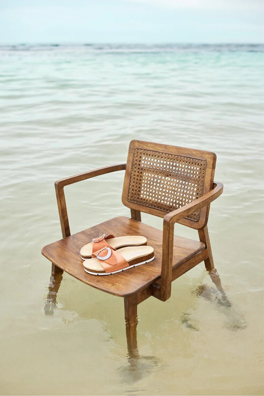 Wooden chair with sandals in shallow water.