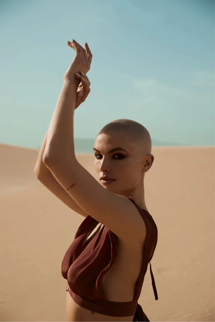 Bald woman with arms raised in the desert.